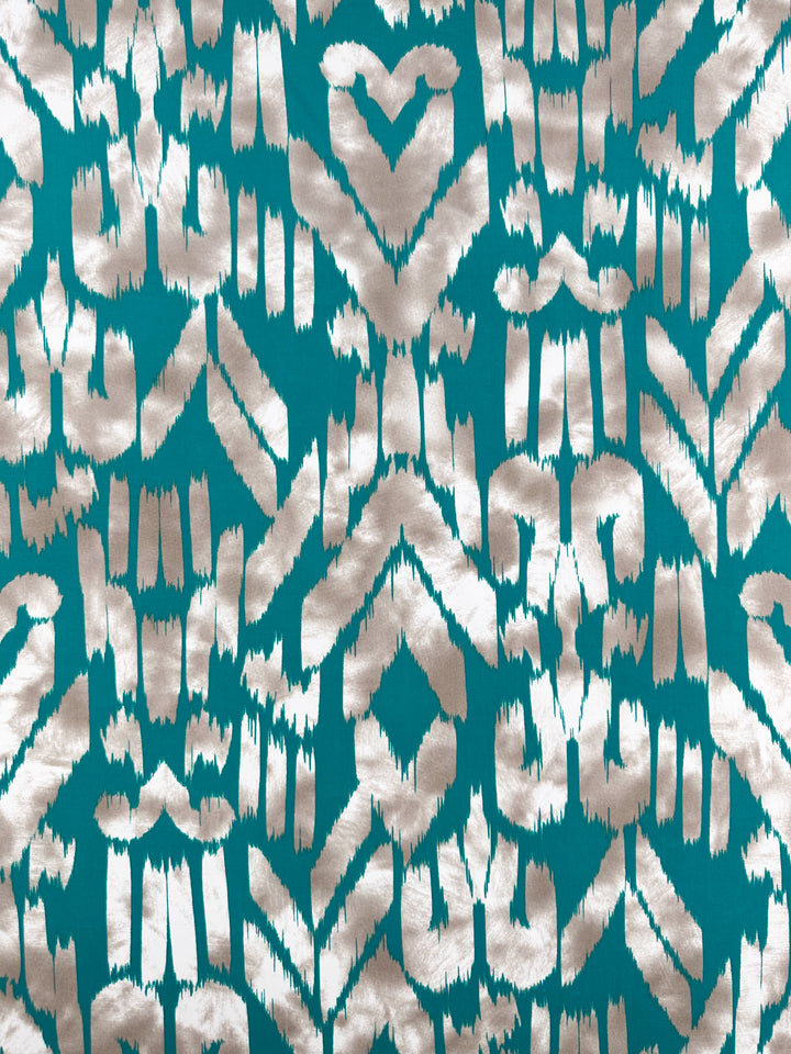 Printed Lycra - Dynasty by Super Cheap Fabrics is a medium-weight, turquoise fabric with white ikat patterns of geometric shapes and zigzags. Made from a Polyester/Spandex blend, it features a symmetrical design with a textured, handcrafted appearance. Width: 150cm.