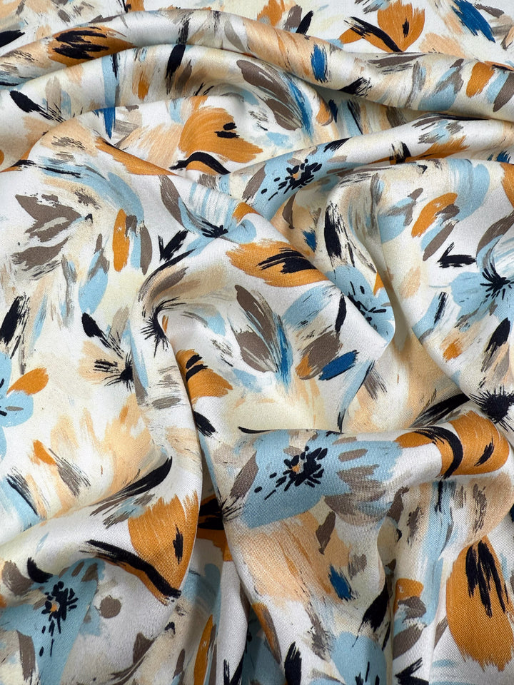 A close-up of Super Cheap Fabrics’ Mercerised Rayon - Autumn Haze (150cm): breathable, lightweight fabric in cream with painterly blue, mustard yellow, black, and beige floral patterns and overlapping brush strokes.