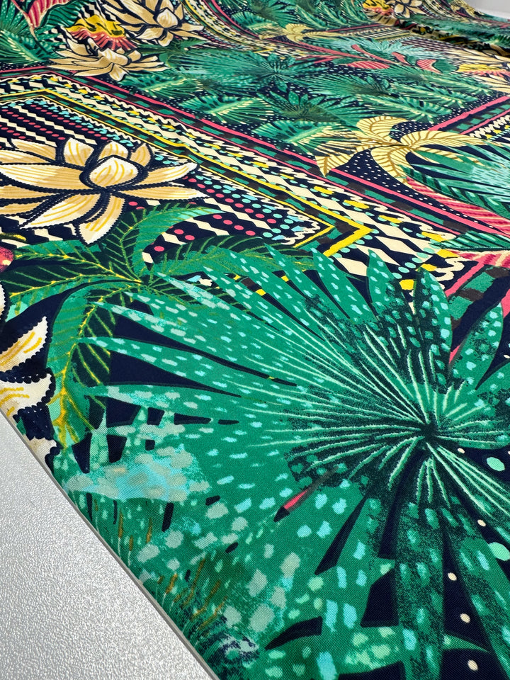 Close-up of Super Cheap Fabrics' "Printed Lycra - Palm Springs - 150cm," a vibrant medium-weight Polyester/Spandex with intricate tropical designs including green palm leaves, yellow flowers, and colorful geometric patterns for a dynamic look.