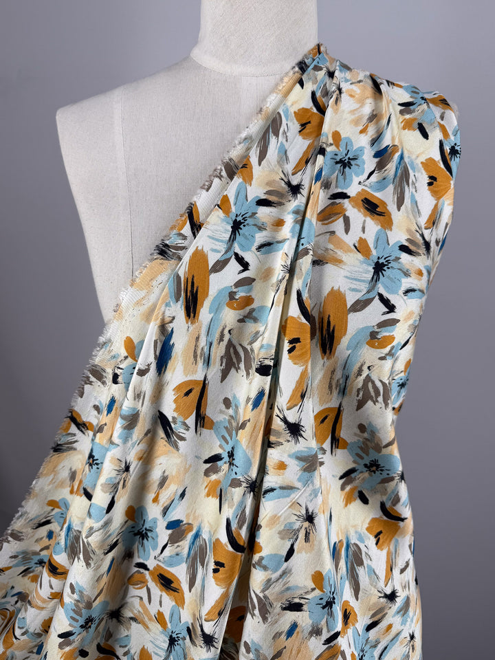 A mannequin displays Super Cheap Fabrics' Mercerised Rayon - Autumn Haze (150cm), a lightweight fabric with a blue, yellow, black, and beige floral pattern, set against a plain gray background.