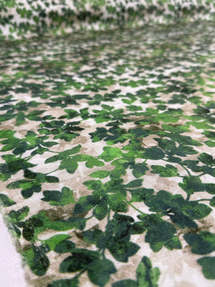 Close-up of Super Cheap Fabrics' Mercerised Rayon - Fig Leaf Camo (150cm): a breathable, lightweight fabric with a dense pattern of overlapping green fig leaves on white, offering a lush, leafy texture.