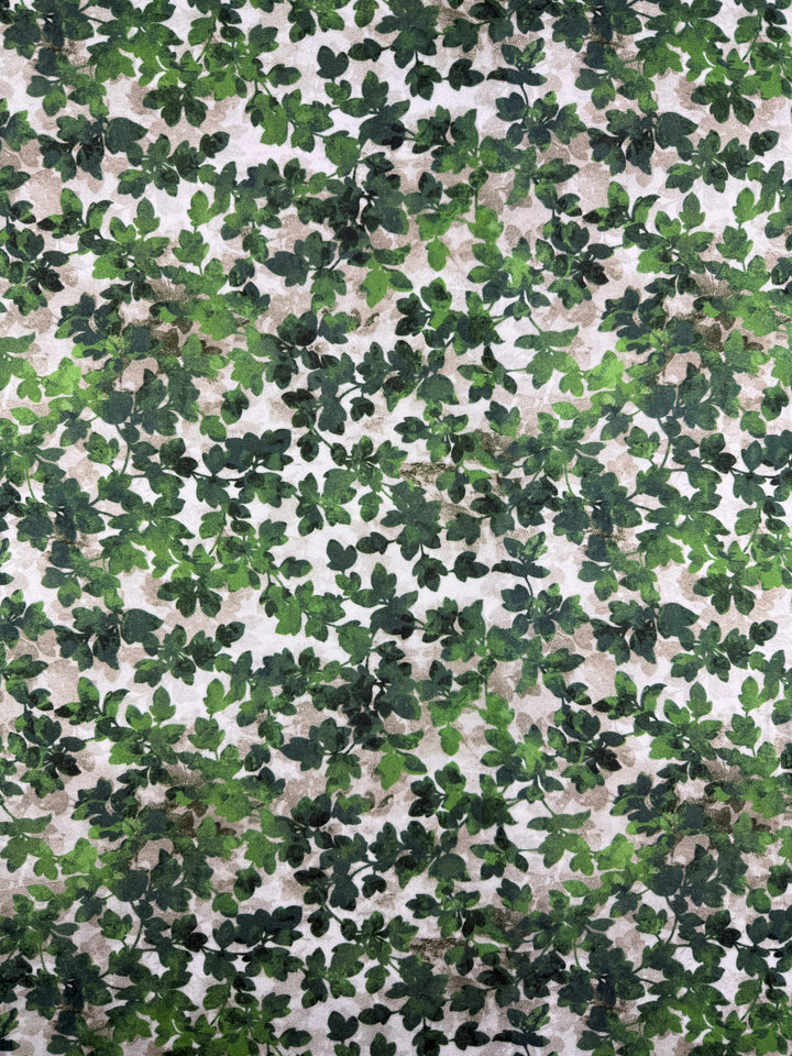 A close-up of Super Cheap Fabrics' Mercerised Rayon - Fig Leaf Camo (150cm), showing its lightweight, breathable fabric with overlapping green, brown, and beige leaf-like shapes in a camouflage pattern.