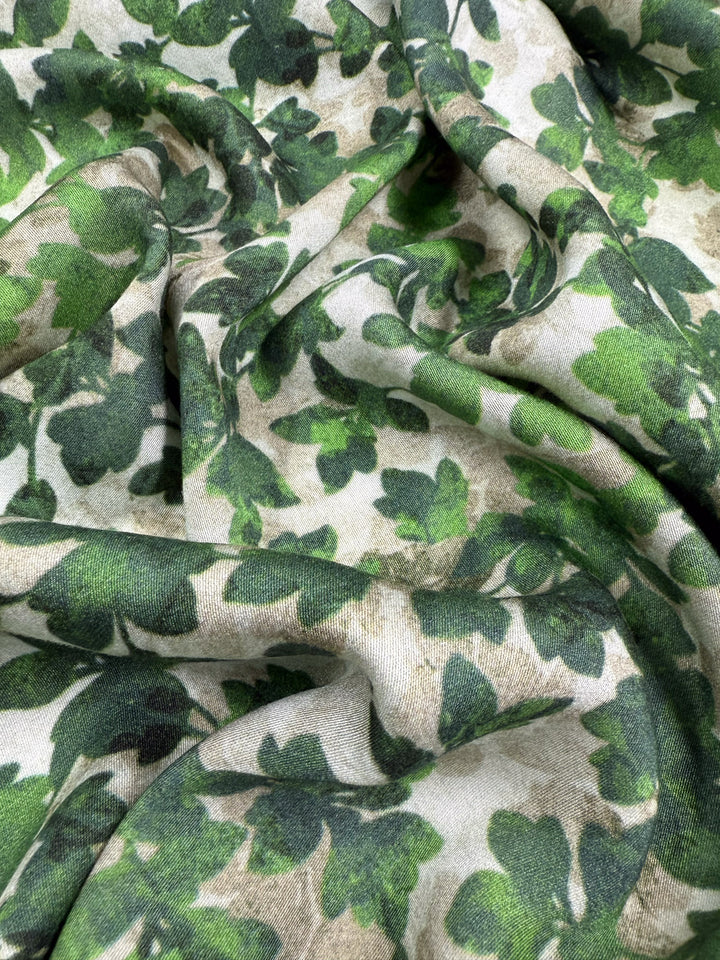 A close-up of Super Cheap Fabrics' Mercerised Rayon - Fig Leaf Camo (150cm), featuring breathable, wrinkle-resistant fabric with green and brown shamrock patterns on a light background.