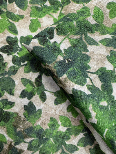 A close-up of Super Cheap Fabrics' Mercerised Rayon - Fig Leaf Camo (150cm), featuring lightweight, breathable fabric with a green and brown leafy camouflage pattern and one corner neatly folded.