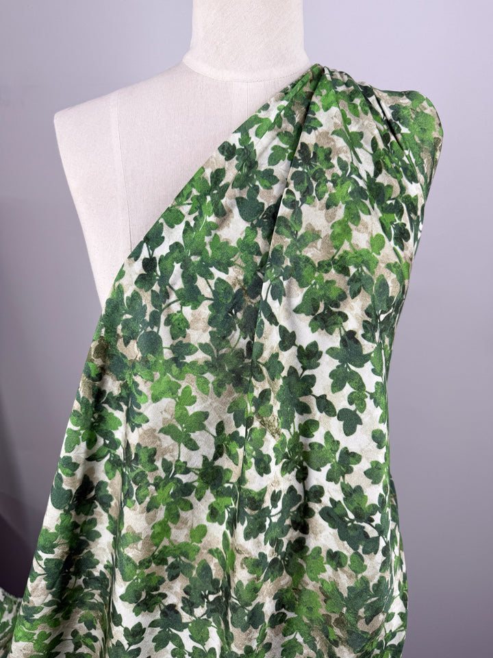 A white mannequin displays Super Cheap Fabrics’ Mercerised Rayon - Fig Leaf Camo (150cm), a lightweight fabric with a green and beige leafy pattern, set against a light gray background.