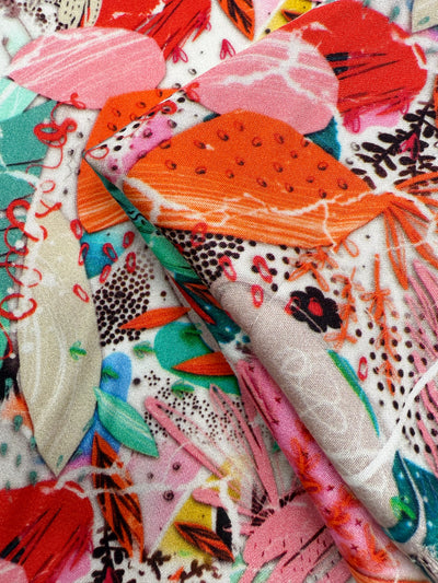 Close-up of Super Cheap Fabrics’ Mercerised Rayon - Electric Orchard (148cm), featuring silky soft, lightweight fabric with bold red, pink, green, orange, and black abstract shapes on a light background.