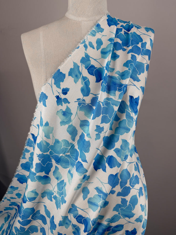 A mannequin displays Super Cheap Fabrics' Mercerised Rayon - Blue Ginkgo (150cm), featuring a blue and turquoise watercolor leaf pattern, against a neutral background.