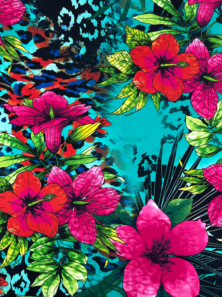 The Super Cheap Fabrics' Printed Lycra - Aqua Flora - 150cm showcases a vibrant design with large pink tropical flowers and green leaves on a dynamic blue, teal, and multicolored abstract background. This medium-weight fabric seamlessly blends bold floral and abstract elements.