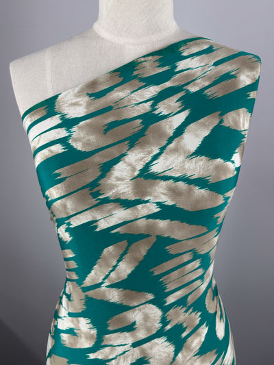 A mannequin showcases a stunning one-shoulder dress in bold teal and silver from Super Cheap Fabrics' Printed Lycra - Dynasty. The abstract pattern of irregular shapes and brush strokes pops against the plain, light gray background, crafted from medium-weight Polyester/Spandex fabric.