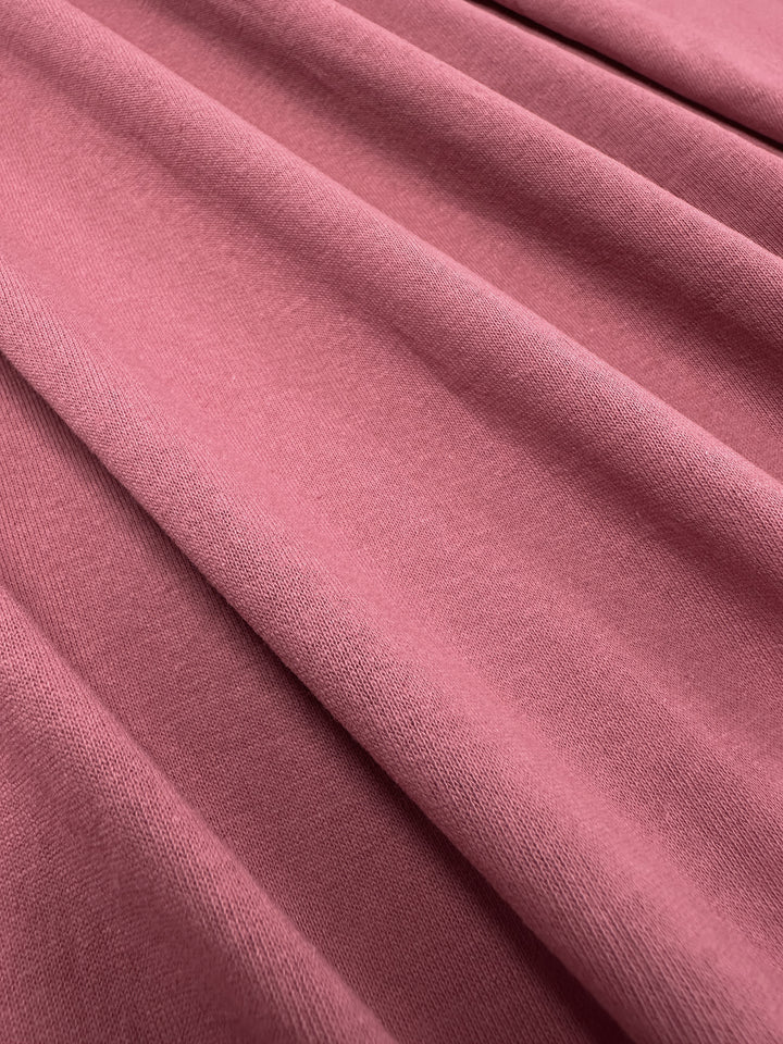 A close-up of Super Cheap Fabrics' Cotton Jersey in Slate Rose, 175cm wide, reveals the smooth texture and subtle sheen of the soft, folded fabric with gentle shadows.