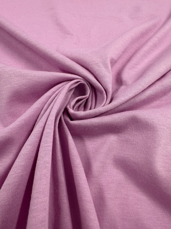 Close-up of Super Cheap Fabrics' pastel lavender cotton jersey (160cm) with a central gathered swirl, forming a textured, spiral pattern. The soft and smooth fabric features subtle shadows that highlight its folds.