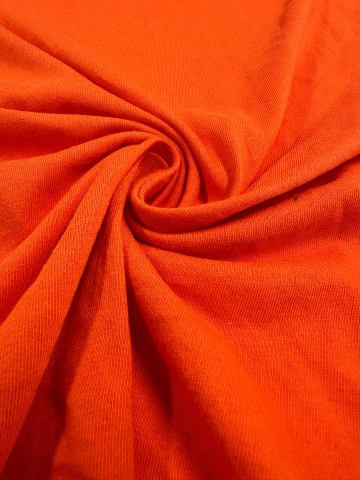 A close-up of Super Cheap Fabrics' Cotton Jersey - Tangerine Tango twists into a spiral, showcasing its light to medium weight softness with a slightly ribbed texture for a dynamic and vibrant look. Measures 155cm.