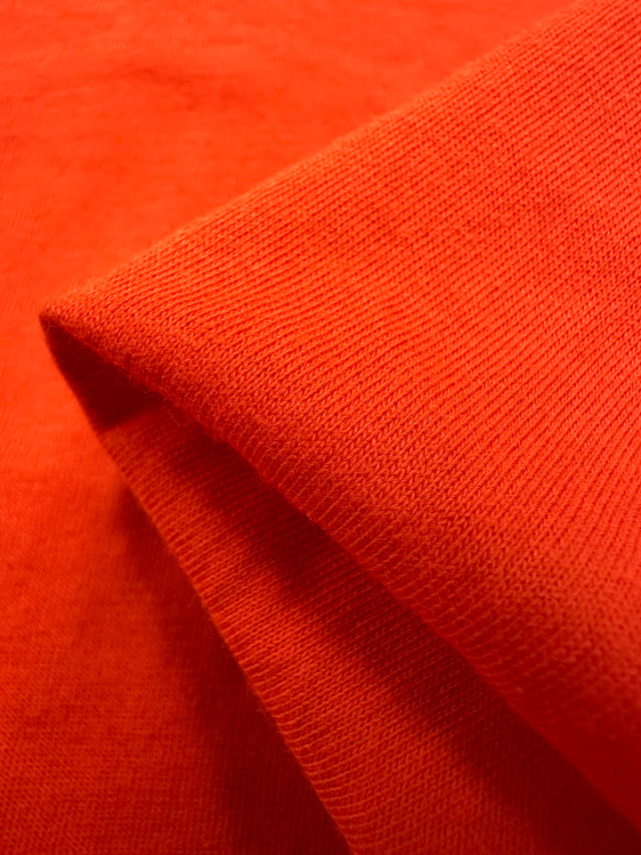 Close-up of Super Cheap Fabrics' Cotton Jersey in Tangerine Tango, featuring a folded corner that highlights its light to medium weight and intricate weave. Width: 155cm.