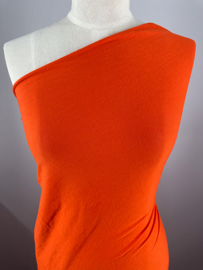 A mannequin displays the Cotton Jersey - Tangerine Tango - 155cm by Super Cheap Fabrics, highlighting its vibrant color and beautiful texture against a neutral background. Crafted from light to medium weight cotton jersey, it showcases an elegant drape.