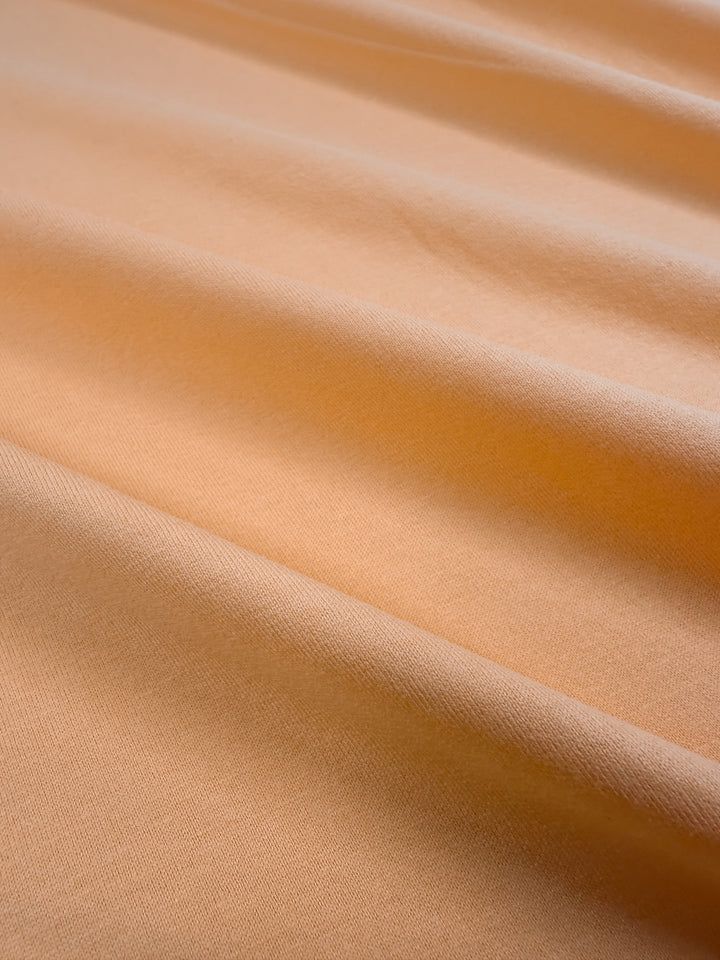 Close-up of smooth, beige Cotton Jersey - Papaya from Super Cheap Fabrics. Gentle folds and soft texture create subtle shadows on this medium-weight material, enhancing its contours. Width: 160cm.