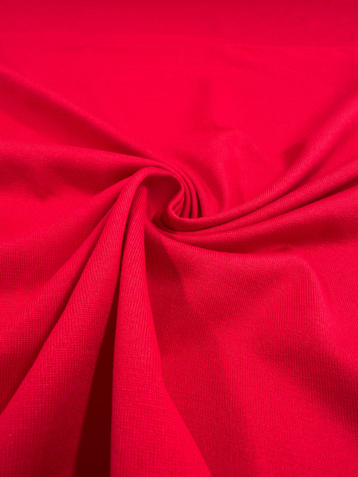 The Cotton Jersey - Ribbon Red from Super Cheap Fabrics features a vibrant hue with a smooth texture, arranged in gentle folds to form a swirling center pattern. This medium-weight 165cm fabric is soft and flowing.