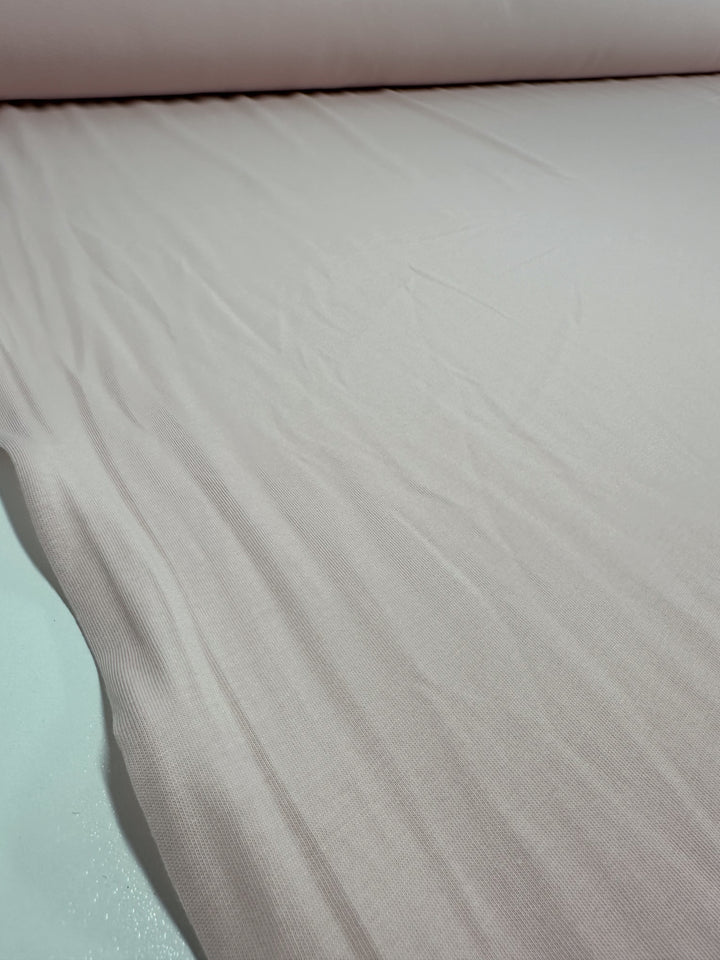 A close-up displays the Super Cheap Fabrics Cotton Jersey in Rosewater, 165cm wide. The light beige fabric has a smooth texture with gentle folds, highlighting its soft and flexible appearance.