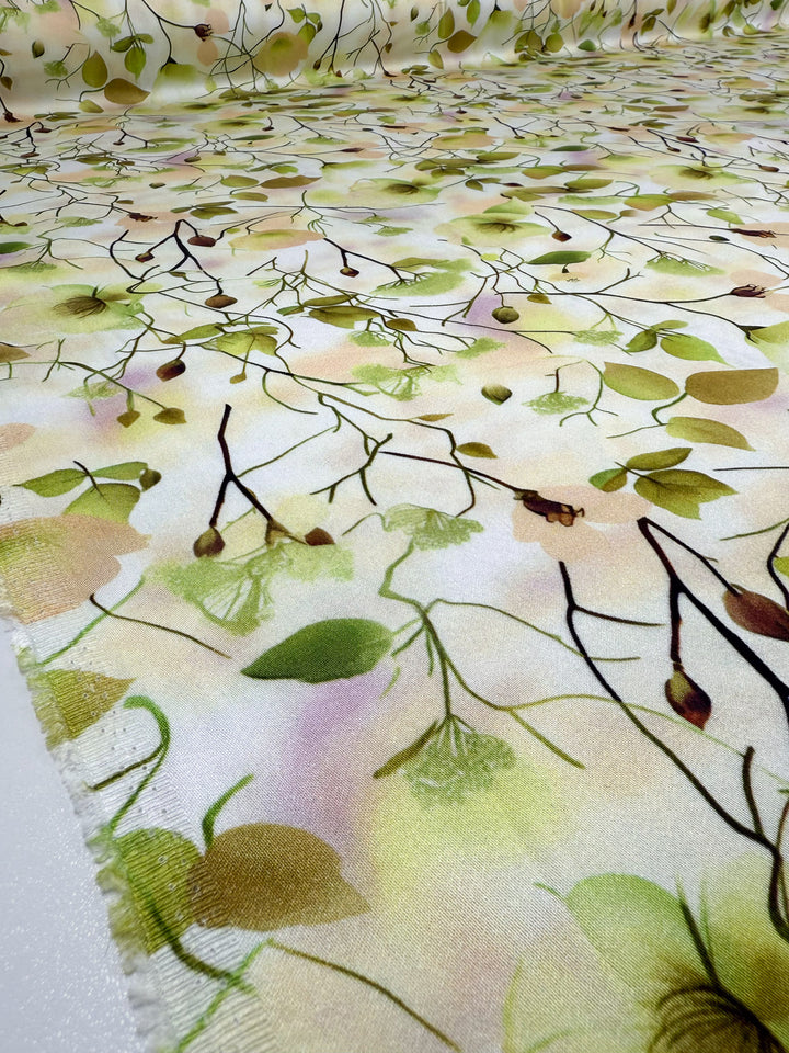 Close-up of Super Cheap Fabrics’ Mercerised Rayon - Sunlit Bouquet (150cm): a lightweight, breathable fabric featuring delicate branches and green leaves on a soft pastel yellow, peach, and green background. Fabric is shown laid out flat.