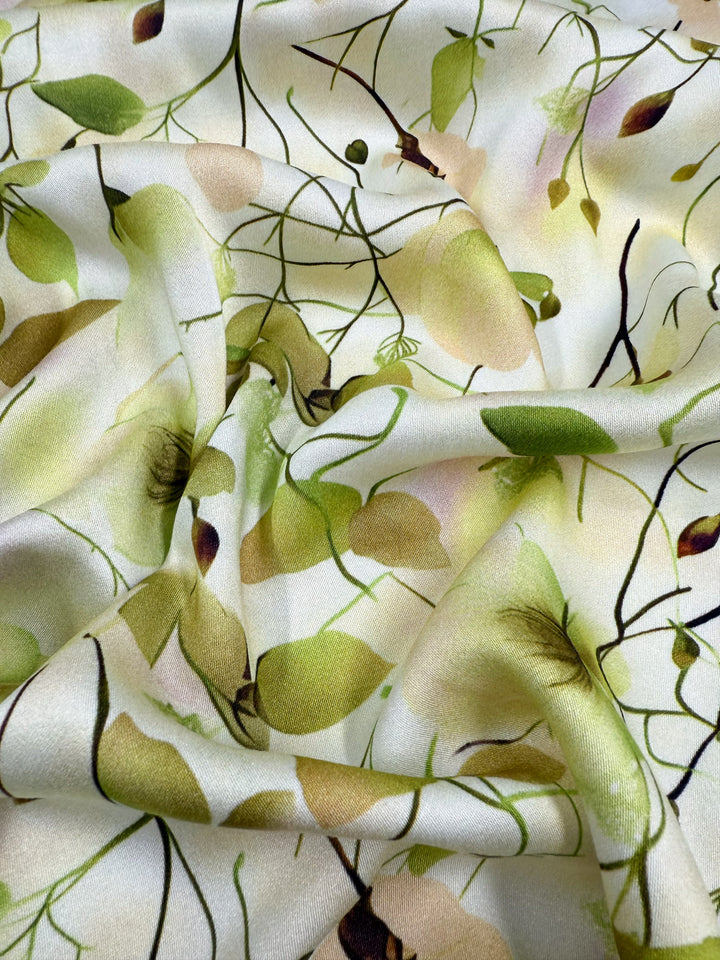 The Mercerised Rayon - Sunlit Bouquet (150cm) from Super Cheap Fabrics features a soft, crumpled texture, light cream base, and a botanical print with green leaves, beige flowers, and black branches—ideal for lightweight, breathable projects.