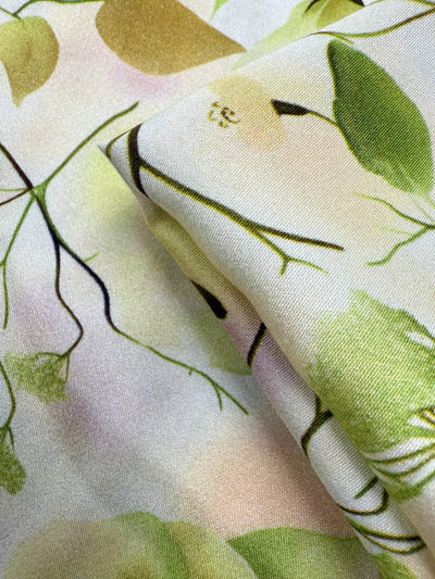 Close-up of Super Cheap Fabrics' Mercerised Rayon - Sunlit Bouquet (150cm): a lightweight, breathable fabric with a nature-inspired pattern of green leaves, yellow fruits, and delicate branches on a white background.