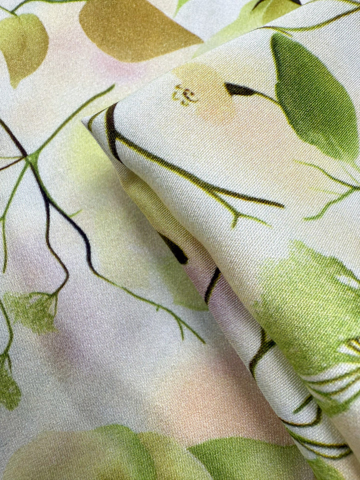 Close-up of Super Cheap Fabrics' Mercerised Rayon - Sunlit Bouquet (150cm): a lightweight, breathable fabric with a nature-inspired pattern of green leaves, yellow fruits, and delicate branches on a white background.
