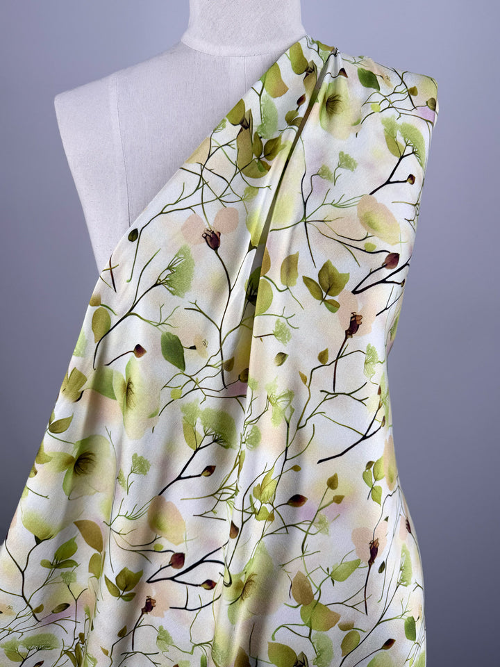 A white mannequin displays Super Cheap Fabrics' Mercerised Rayon - Sunlit Bouquet (150cm), a lightweight, breathable fabric with a light green, yellow, and brown botanical print of delicate leaves, branches, and buds for a soft, nature-inspired look.