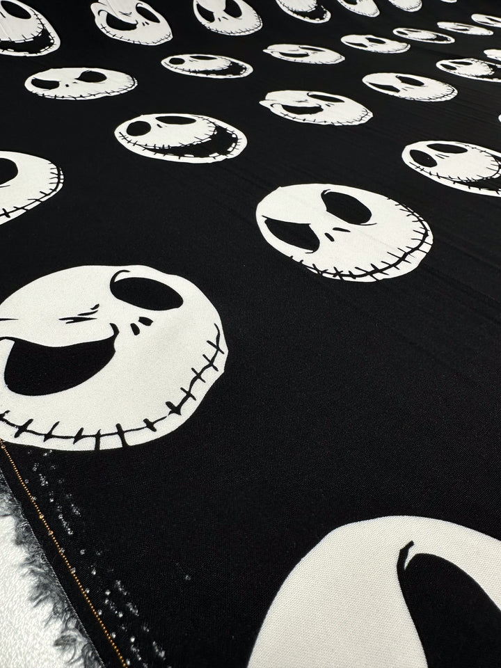 The Printed Rayon - Skellington - 140cm from Super Cheap Fabrics features a whimsical Halloween theme with vibrant white cartoon-style skulls on black fabric, complete with stitched mouths and dark eye sockets, capturing a playful spirit.