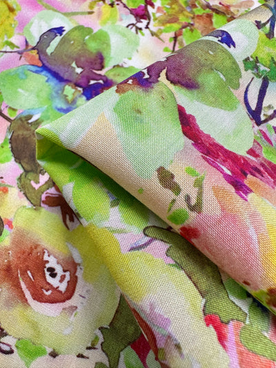 A close-up of the Designer Rayon - Sierra by Super Cheap Fabrics displays a vibrant, floral pattern with pink, green, yellow, and red watercolor-style hues. Slightly folded, it showcases its colorful design on a 145cm versatile fabric.