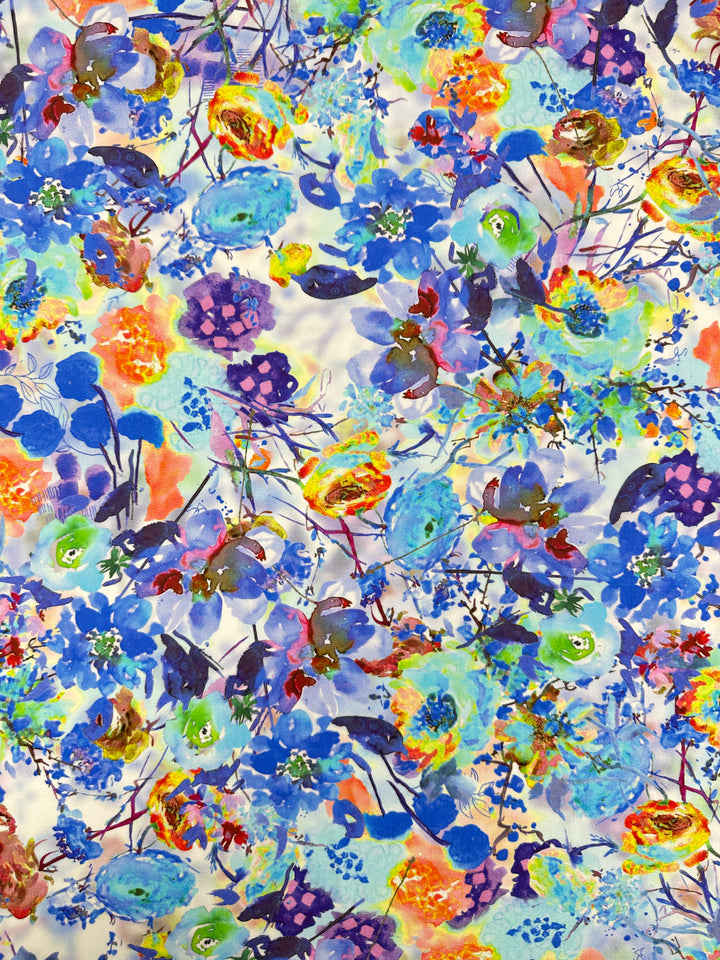 The Designer Rayon - Cortney - 145cm fabric by Super Cheap Fabrics showcases a dense floral pattern with vibrant blue, orange, yellow, and purple flowers and green leaves. This versatile choice offers colorful, abstract designs for a lively and energetic feel.