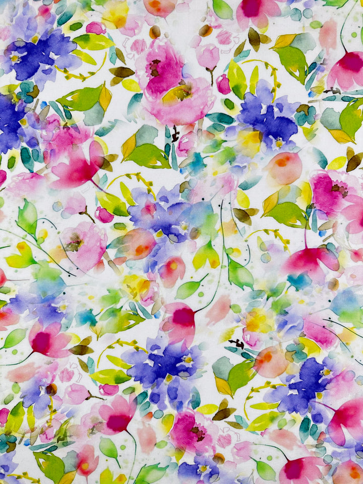 The Designer Rayon - Milana from Super Cheap Fabrics features a vibrant watercolor floral pattern with clusters of pink, blue, and yellow flowers and green leaves on white. This lively design is versatile for rayon fabric, adding a joyful, natural feel to any space. Width: 145cm.