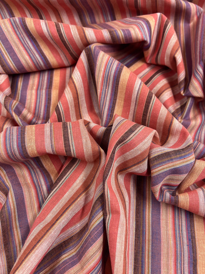 The Linen Blend - Colombo - 150cm fabric by Super Cheap Fabrics, featuring yarn-dyed stripes in vibrant shades of pink, orange, red, purple, and beige, is elegantly draped and folded to create subtle waves and textures.