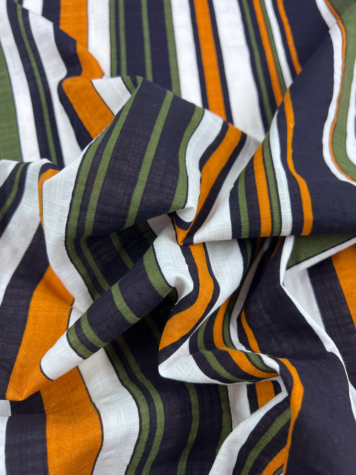 A close-up of the Linen Blend - Retro - 145cm from Super Cheap Fabrics showcases breathable fabric with bold vertical stripes in black, white, orange, and green. Gently gathered into folds, this fabric presents a textured appearance ideal for creating stylish summer outfits.