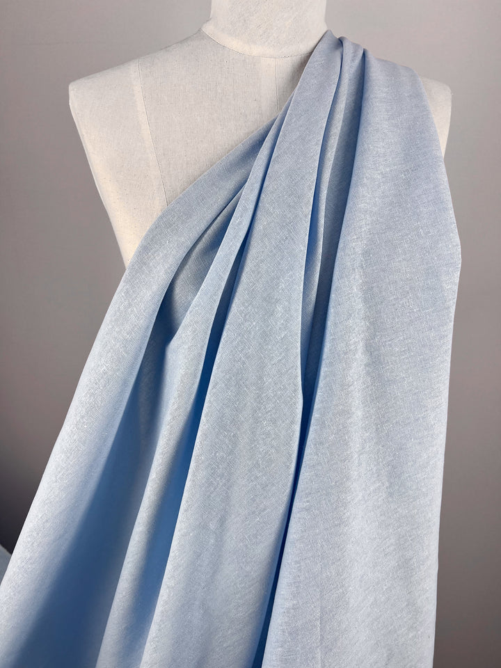 A piece of the Premium Linen Cotton - Clear Sky - 140cm from Super Cheap Fabrics is elegantly draped over a mannequin, highlighting its soft texture and gentle folds. The simple, neutral background resembles a clear sky, emphasizing the fabric's color and smoothness.