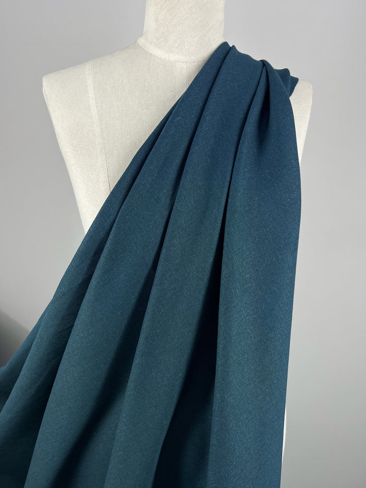 A mannequin draped with Premium Linen Cotton - Balsam from Super Cheap Fabrics against a neutral background highlights the texture and elegant hue of the dark teal fabric, showcasing its lightweight quality.