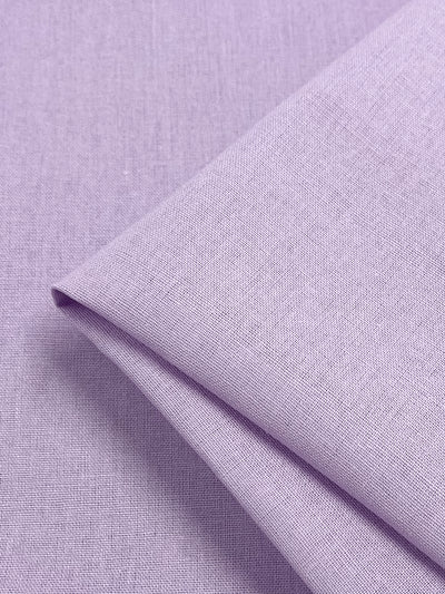 A close-up of a folded piece of Super Cheap Fabrics' Premium Linen Cotton in "Orchid Bouquet," illustrating its texture and weave. The smooth, tightly woven surface of the 140cm fabric creates delicate shadows with its visible folds, invoking the elegance of an orchid bouquet.