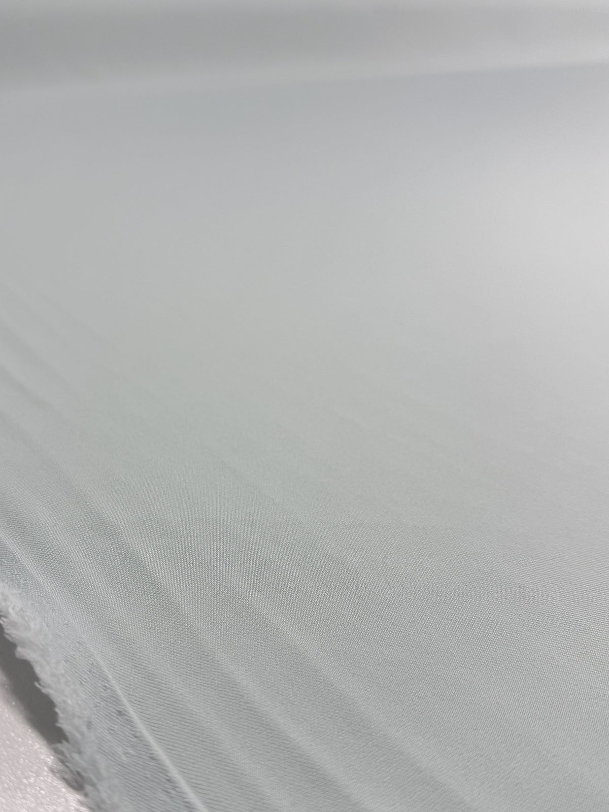 A close-up of Super Cheap Fabrics’ Liquid Twill - Murmur (150cm), featuring its light grey, smooth yet slightly textured surface with visible edges and soft folds.