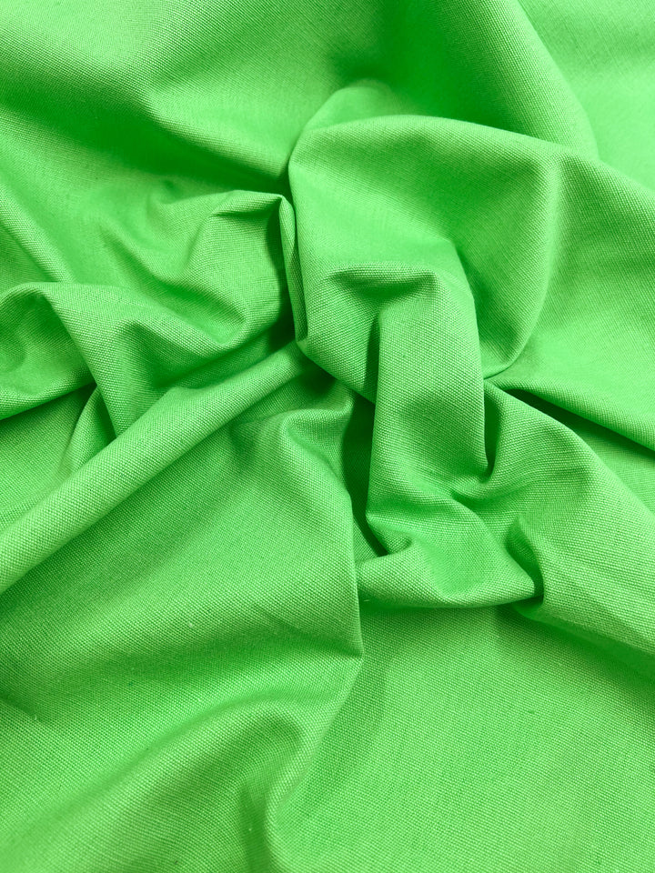 A close-up of Super Cheap Fabrics' Linen Blend in Summer Green, 150cm wide, displays its smooth texture, gathered and crumpled at the center to create soft folds and shadows. This medium-weight fabric lends gentle elegance to any design.