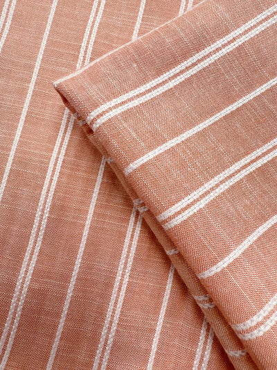 Close-up of Super Cheap Fabrics' Linen Blend - Dusty Blush Ticking (142cm), light brown with white vertical stripes, showing a folded section on top of a flat piece to highlight the woven texture and pattern.