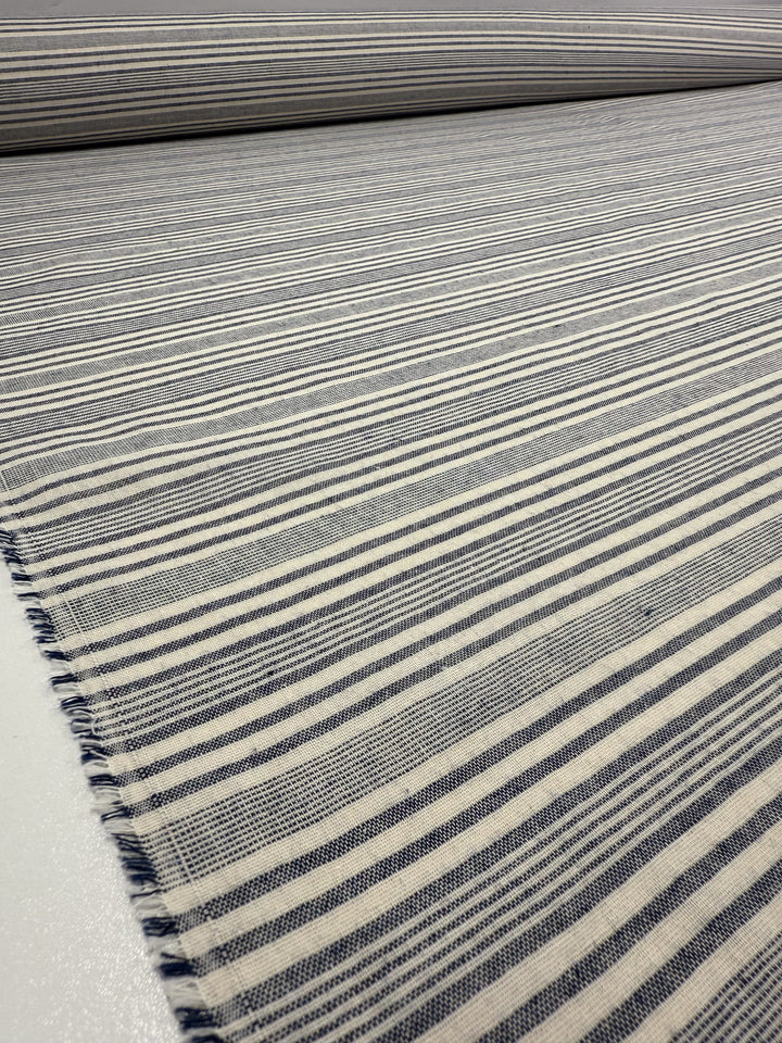 A close-up of Super Cheap Fabrics’ Linen Blend - Coastal Navy Stripe (140cm), showing blue and white uneven horizontal stripes on cotton linen fabric, laid flat with a slightly frayed edge in the foreground.