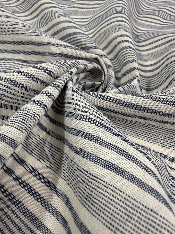 A close-up of Super Cheap Fabrics’ Linen Blend - Coastal Navy Stripe (140cm), showing light beige fabric with navy stripes, a subtle texture, and a gathered, slightly twisted center section.