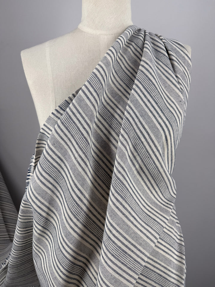 A fabric mannequin is draped in Super Cheap Fabrics’ Linen Blend - Coastal Navy Stripe (140cm), shown from the shoulders down with the striped material wrapped diagonally across the chest. The background is plain gray.