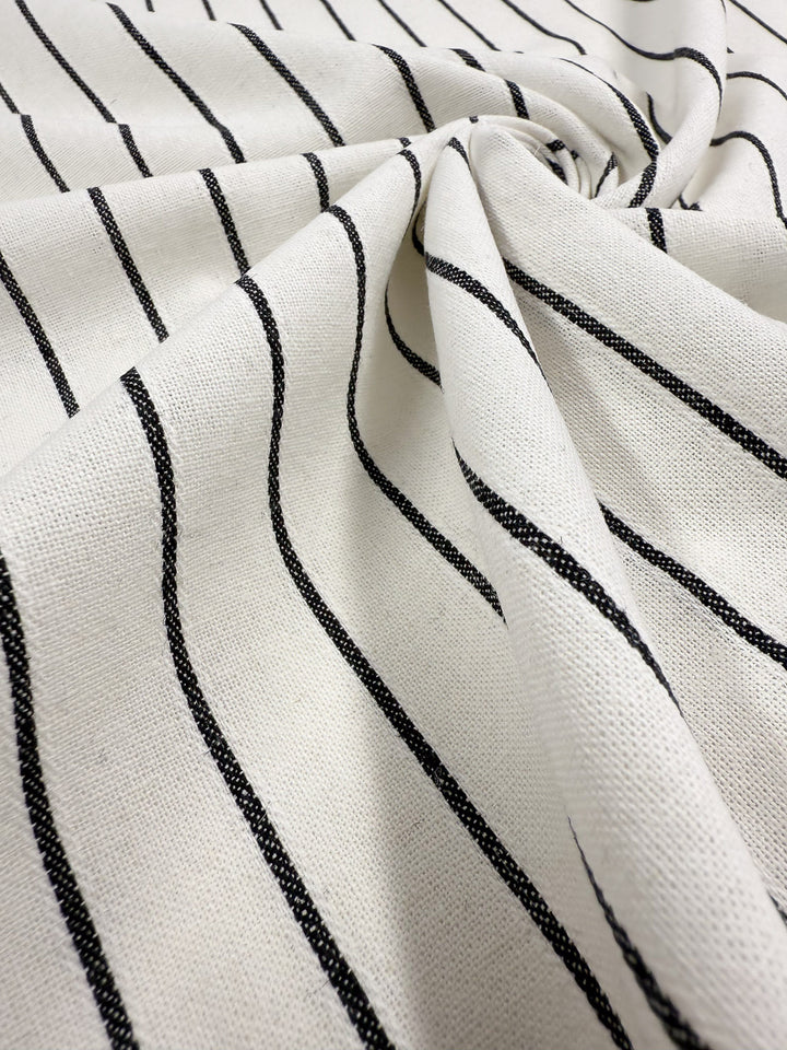 A close-up of Super Cheap Fabrics' Linen Blend - Classic Chalk Pinstripe (135cm), a cream-colored, lightweight linen cotton blend with thin black stripes, softly gathered and twisted to create gentle folds and curves.