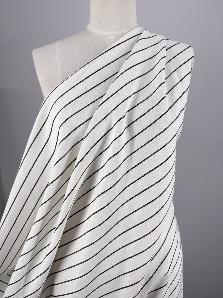 A mannequin displays Super Cheap Fabrics’ Linen Blend - Classic Chalk Pinstripe (135cm), featuring thin, evenly spaced black diagonal stripes on white, set against a plain gray background.