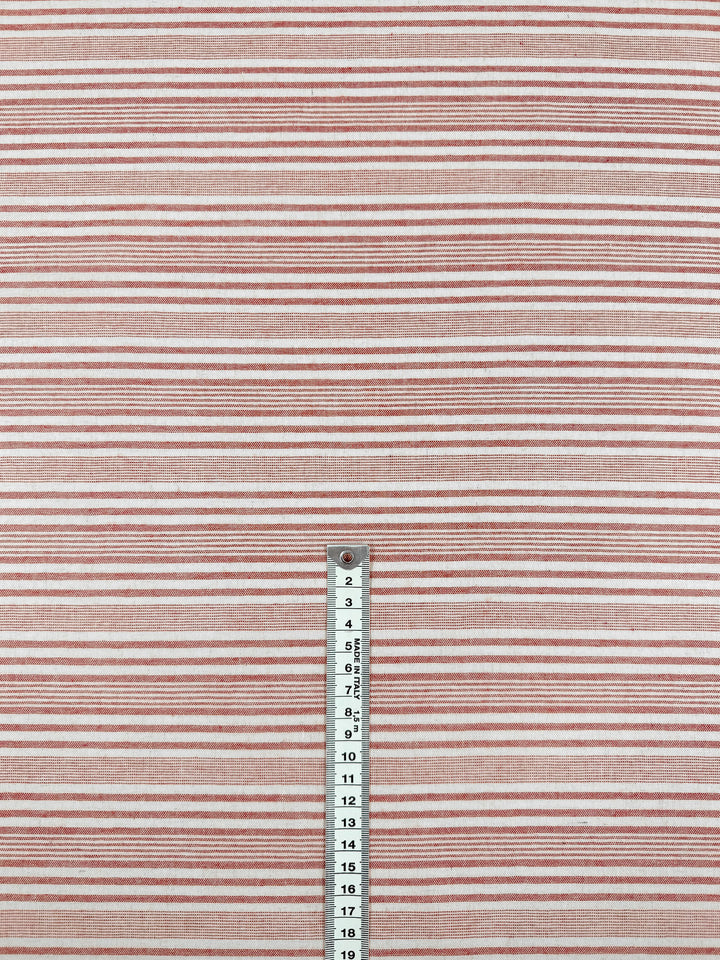 A metal ruler (centimeters 2–18) stands vertically, measuring Super Cheap Fabrics' Linen Blend - Rosebay Stripe - 145cm, a lightweight linen fabric featuring horizontal red, pink, and white stripes.