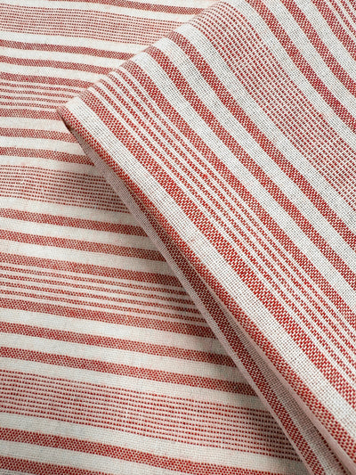 Close-up of Super Cheap Fabrics' Linen Blend - Rosebay Stripe (145cm): red and white striped lightweight fabric with varying stripe thickness, soft texture, and overlapping layers highlighting its woven detail.