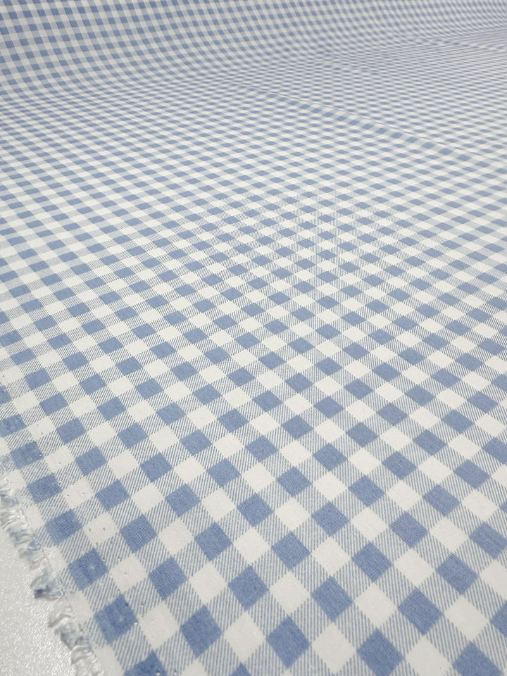 A close-up of Super Cheap Fabrics’ Linen Blend - Powder Blue Picnic (140cm) shows its soft, lightweight blue and white gingham check pattern—perfect for summer jackets. The slightly wrinkled fabric reveals a neat grid of small squares.