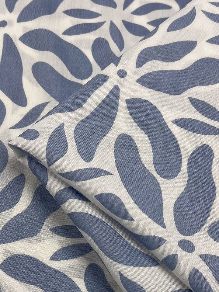 A close-up of folded Designer Rayon Chambray Blue from Super Cheap Fabrics showcases vibrant abstract, blue floral or leaf prints on white. The symmetrical and evenly spaced design is modern and artistic, offering a versatile choice. Width: 140cm.