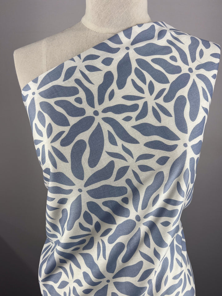 A mannequin showcases Super Cheap Fabrics' Designer Rayon - Chambray Blue, featuring a blue and white abstract floral pattern with leaf-like shapes against gray, adding modern elegance to any setting.