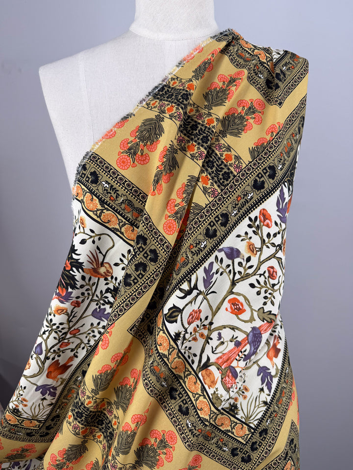 A mannequin displays Super Cheap Fabrics’ Designer Rayon - Antique Tapestry (145cm), a soft, lightweight rayon in yellow and cream with vibrant floral, bird, and geometric patterns in orange, black, purple, and green.