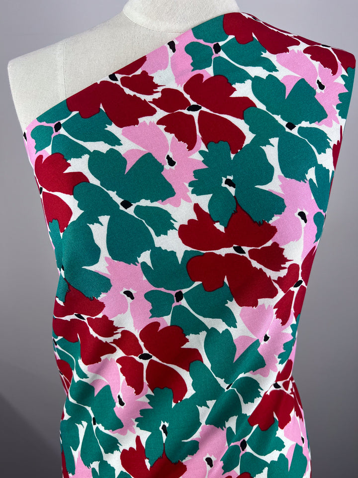 A mannequin displays Super Cheap Fabrics' Designer Rayon - Spring (140cm) with a bold, abstract floral pattern in red, green, and pink. The vibrant design covers the entire surface and is eye-catching and versatile.